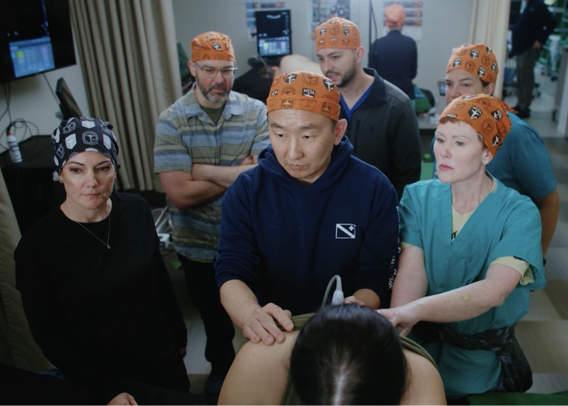 Five students and a professor practicing ultrasound skills on a patient's back